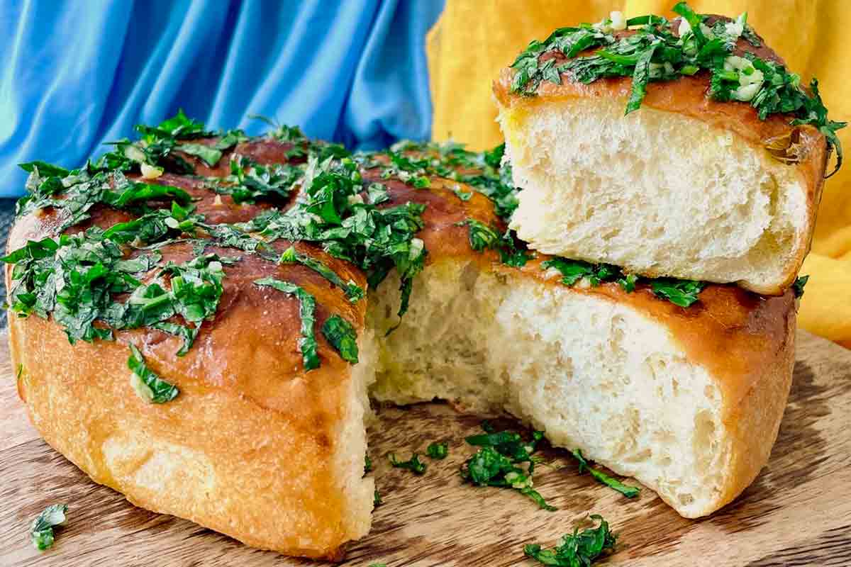 A piece of Ukrainian garlic bread pulled apart from the whole loaf, topped with parsley and garlic.