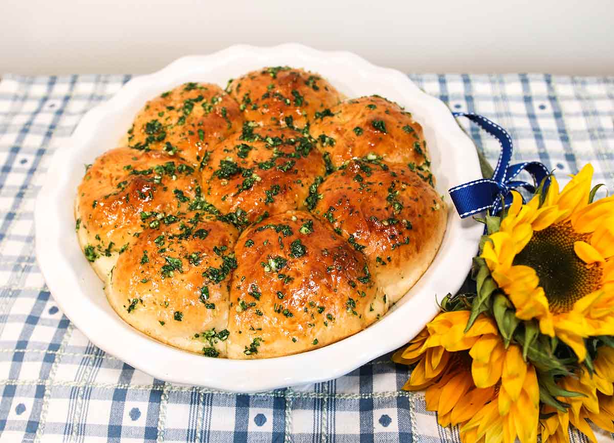 Eight Ukrainian garlic bread rolls on a white plate with a bunch of sunflowers on the side