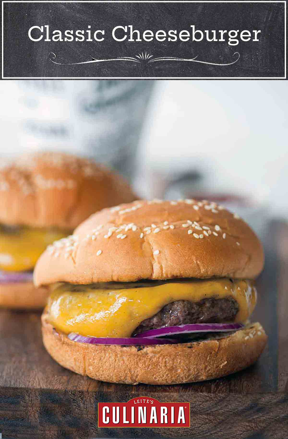 Two classic cheeseburgers with red onion and pickles on sesame buns on a wooden serving board.