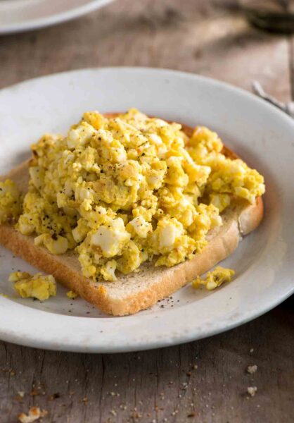 A slice of bread topped with egg salad without mayo n a white plate.