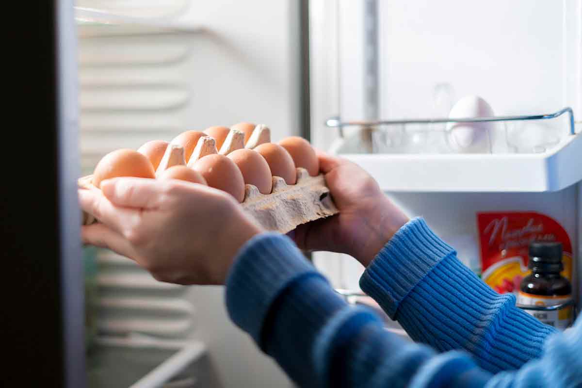 A woman placing a dozen raw eggs in the refrigerator