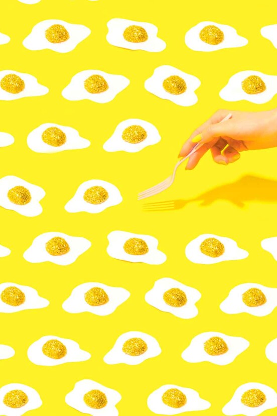 Yellow background with any fried eggs and a woman's hand with a fork
