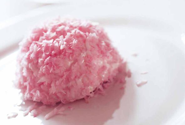 A pink homemade sno ball--coconut-covered dome--on a white plate with two more in the back