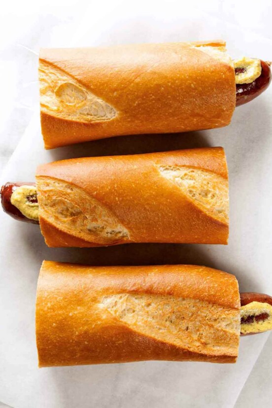 Three servings of hot dog on a baguette with mustard on a paper napkin.