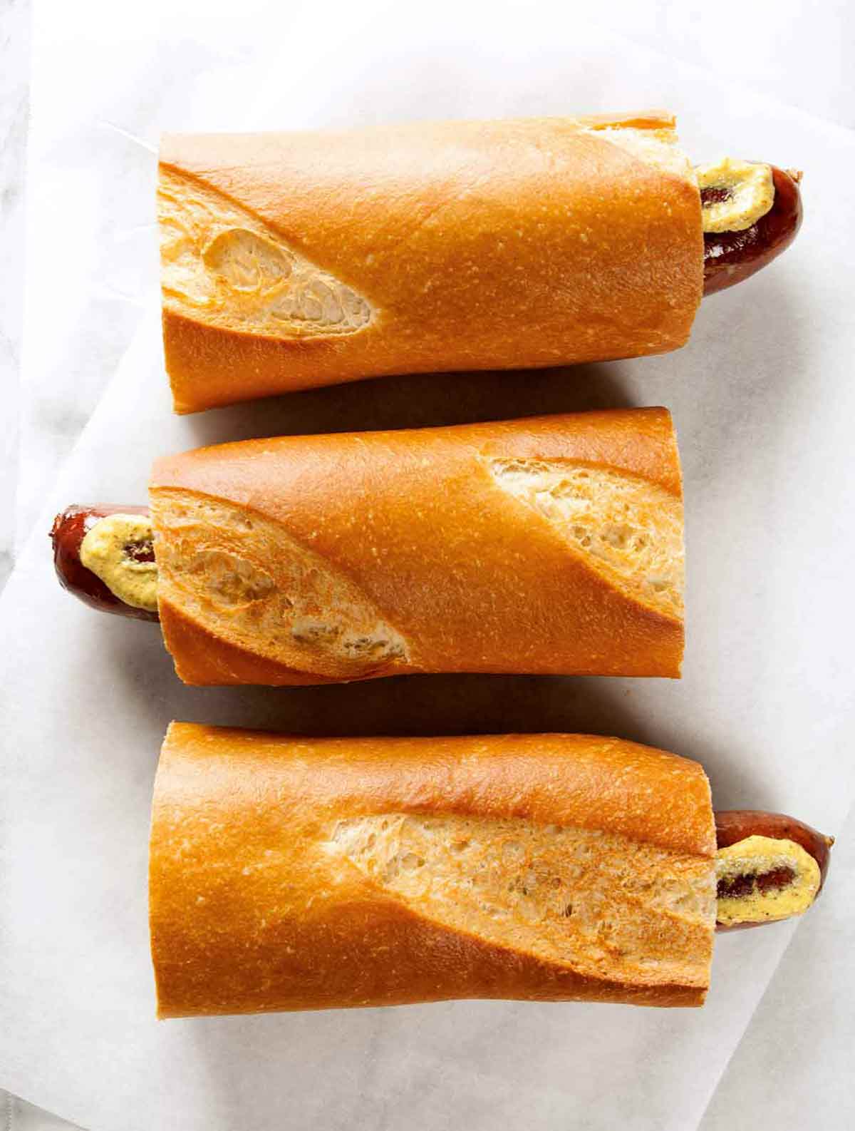 Three servings of hot dog on a baguette with mustard on a paper napkin.