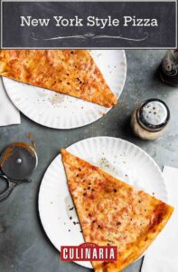 Two slices of New York style pizza on paper plates with a cheese shaker and napkins beside the pizza.