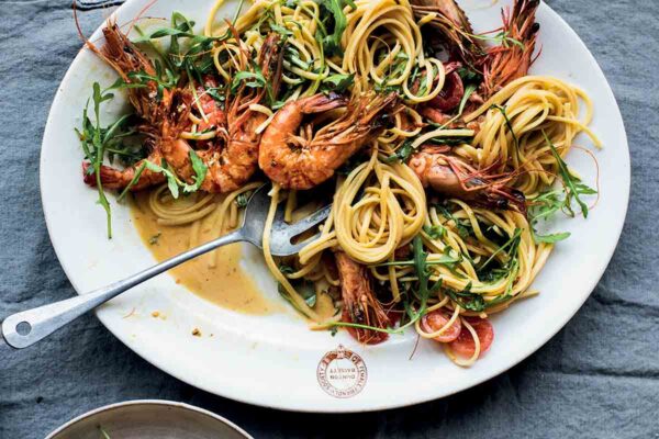 A large white plate full of turmeric shrimp linguine with a serving spoon resting in it.