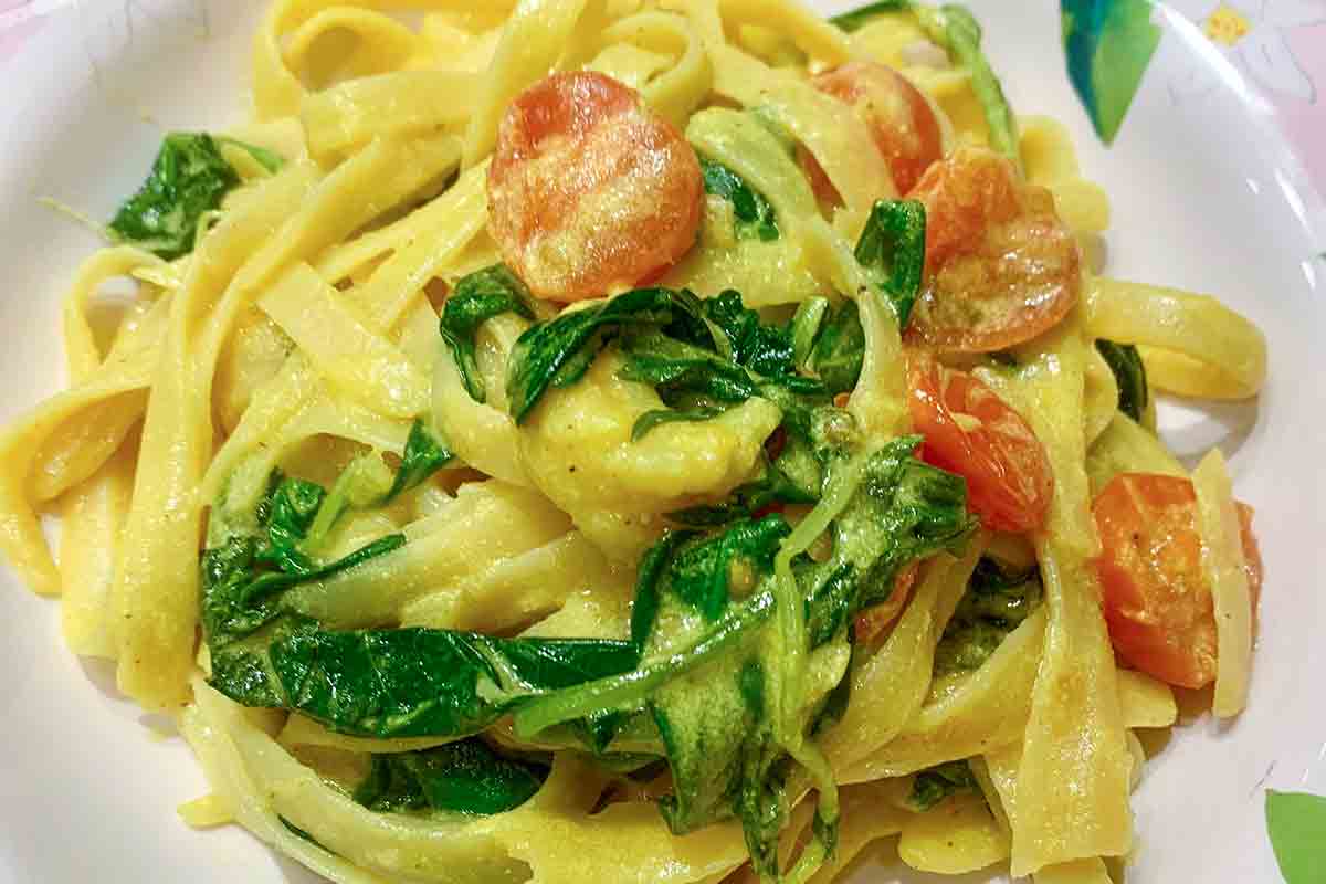 A white plate filled with turmeric shrimp linguine and wilted arugula