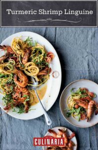A large white plate full of turmeric shrimp linguine with a serving spoon resting in it.