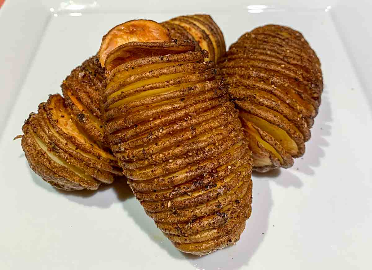 Three air fryer hasselback potatoes piled on a white square plate.