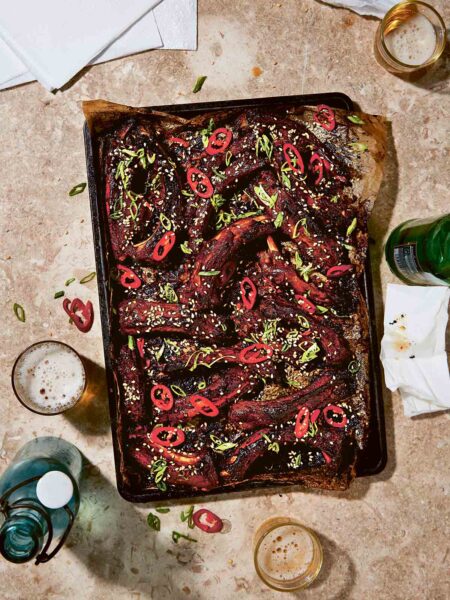 Individual Asian sticky ribs on a baking sheet topped with sliced chile, scallions, and sesame seeds
