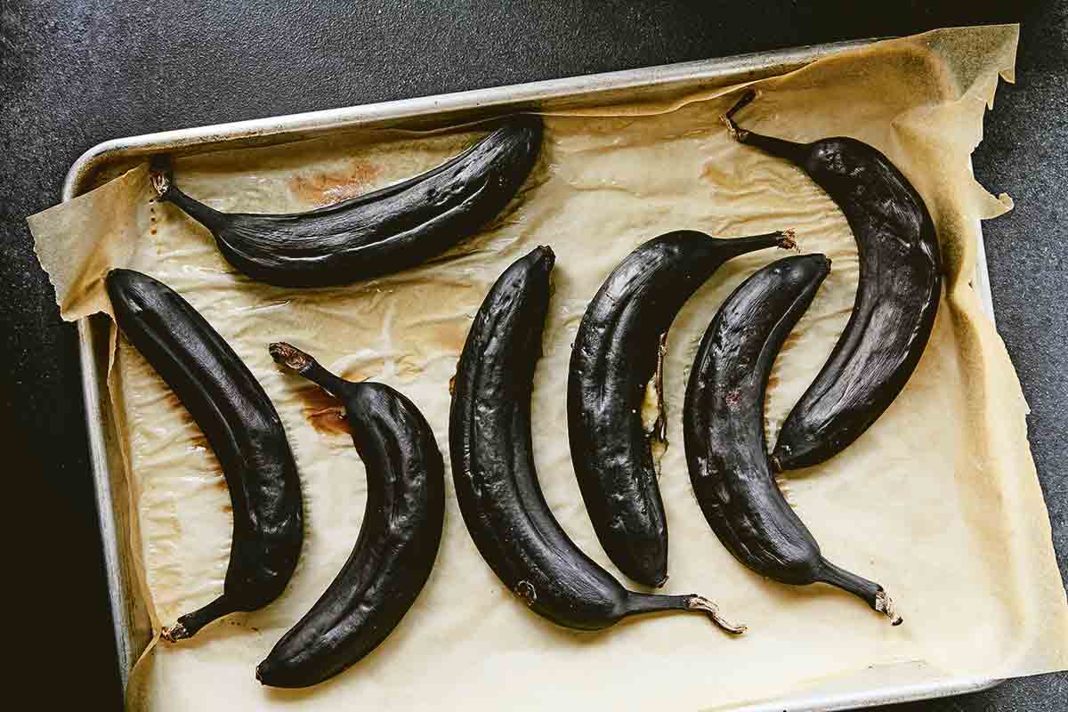 A sheet pan lined with parchment and seven black bananas.