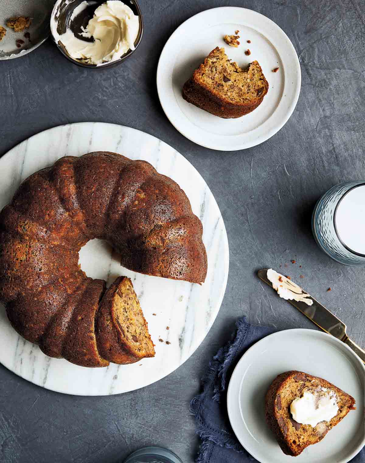 A Bundt banana bread on a white serving platter and individual slices on two plates.