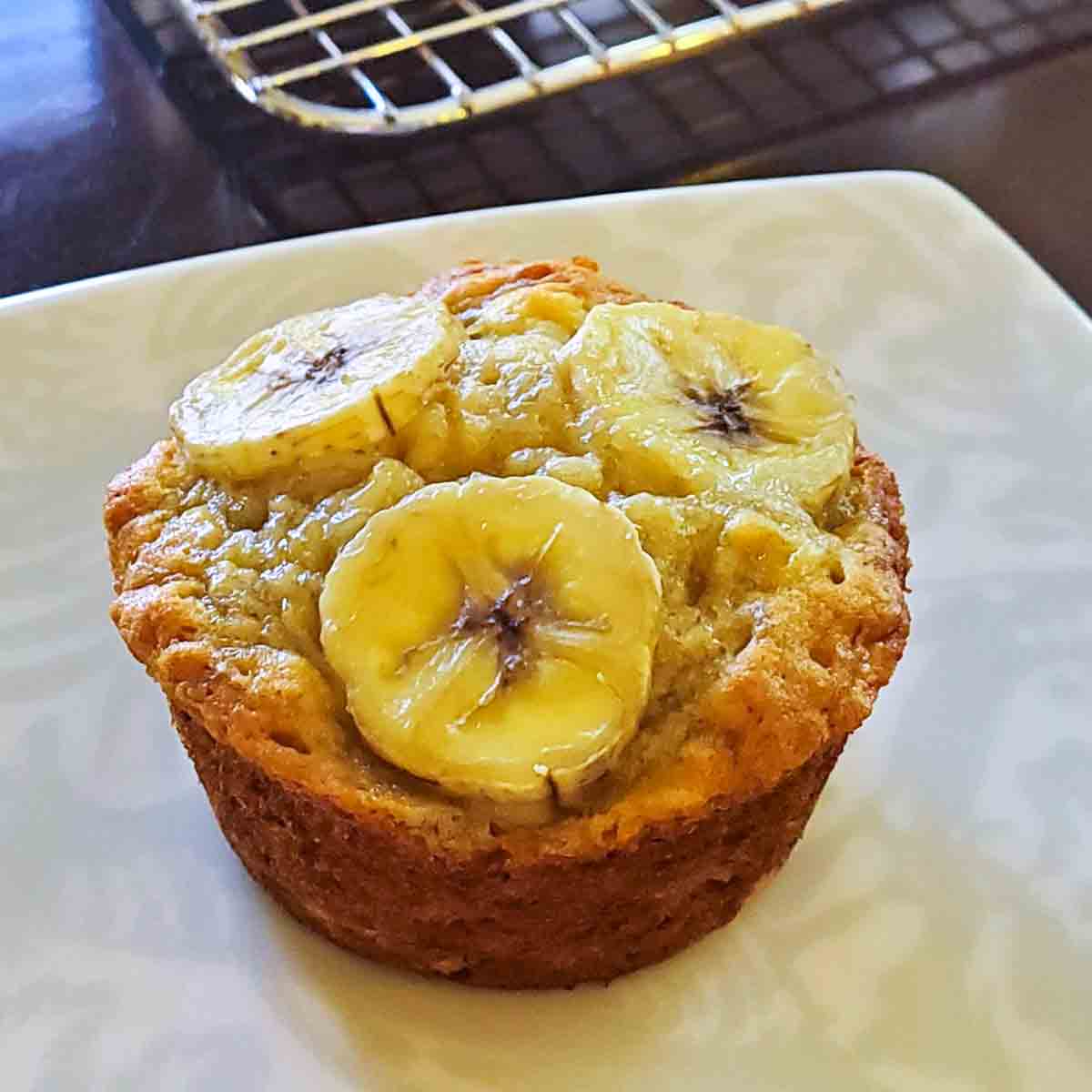 A single banana topped muffin on a white plate.