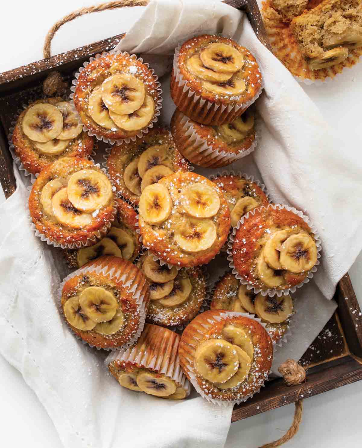 A wooden box filled with banana topped muffins.