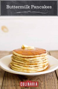 A stack of fluffy buttermilk pancakes on a white plate with syrup and butter on top.