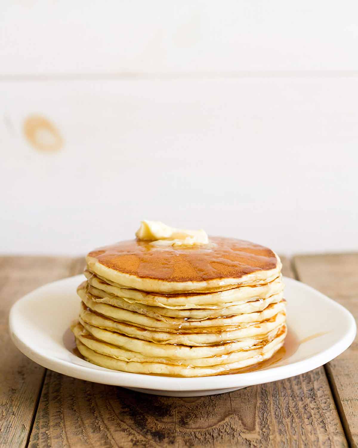 A stack of fluffy buttermilk pancakes on a white plate with syrup and butter on top.