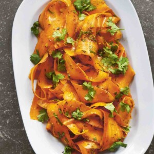 A white oval serving platter filled with carrot ribbon salad and garnished with cilantro leaves.