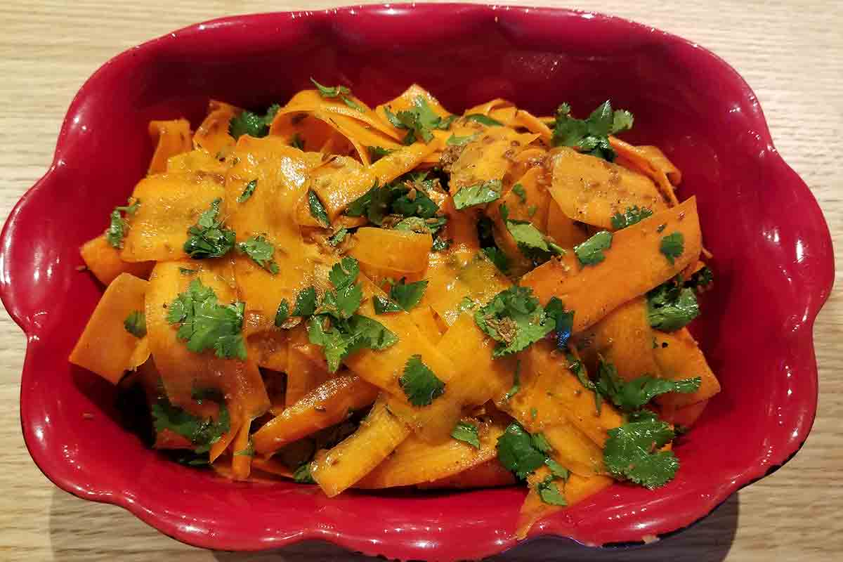 A red scalloped serving dish filled with carrot ribbon salad, topped with cilantro.