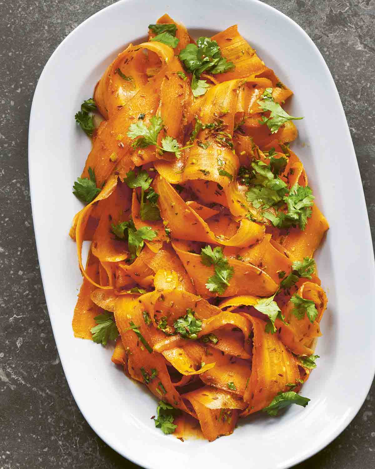 A white oval serving platter filled with carrot ribbon salad and garnished with cilantro leaves.