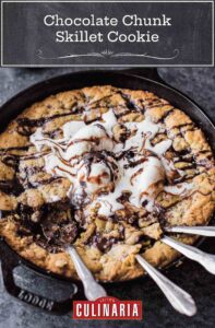 A large chocolate chip skillet cookie topped with ice cream with four spoons resting inside.