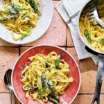 Two bowls filled with creamy asparagus pasta with a pot of pasta on the side