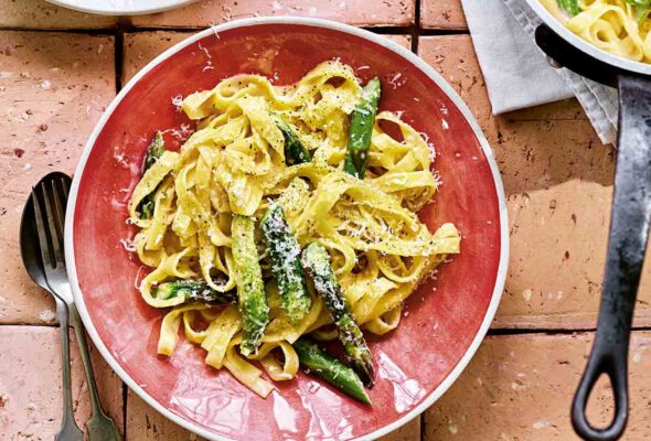 Two bowls filled with creamy asparagus pasta with a pot of pasta on the side