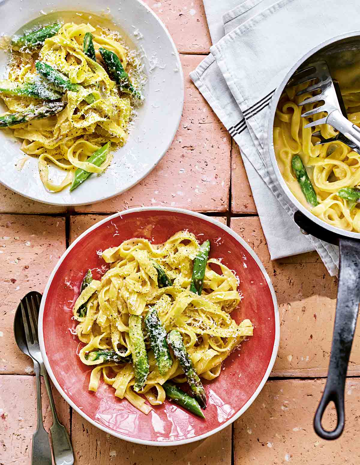 Two bowls filled with creamy asparagus pasta with a pot of pasta on the side