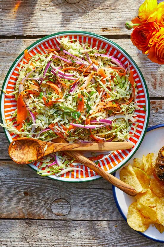 A colorful serving platter filled with coleslaw with cilantro with wooden serving utensils on the side.