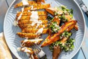 A crispy chicken schnitzel cutlet on a plate with sweet potato wedges and a herb vinaigrette