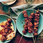 Three easy marinated chicken skewers on a blue plate and a fourth one on top of a piece of flatbread.