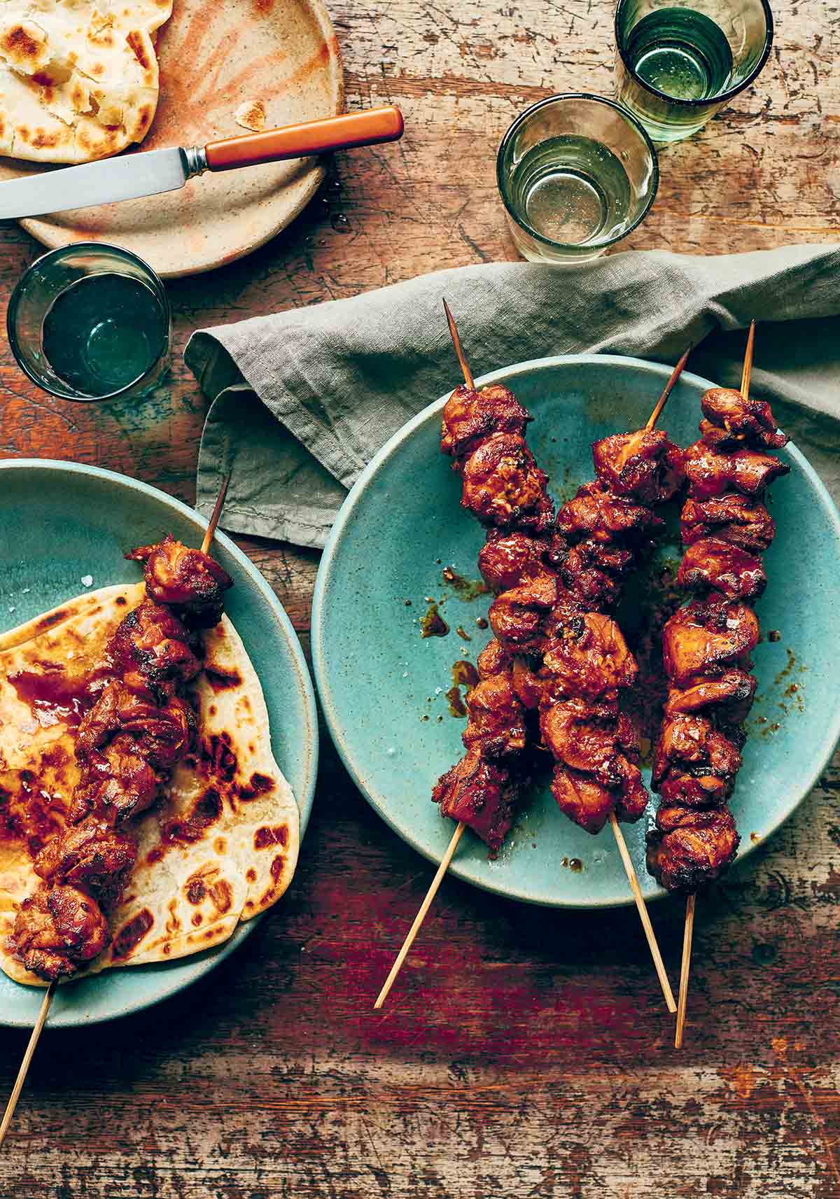 Three easy marinated chicken skewers on a blue plate and a fourth one on top of a piece of flatbread.