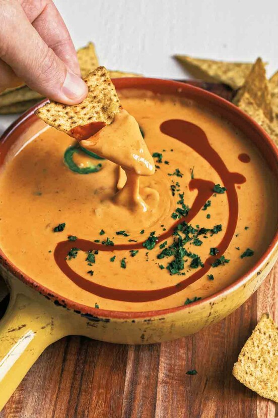 A bowl of easy queso dip with a person dipping a chip into it