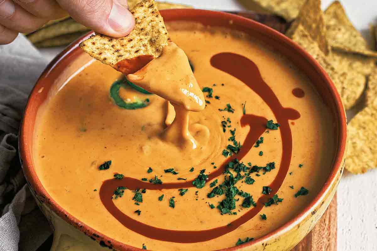 A bowl of easy queso dip with a person dipping a chip into it