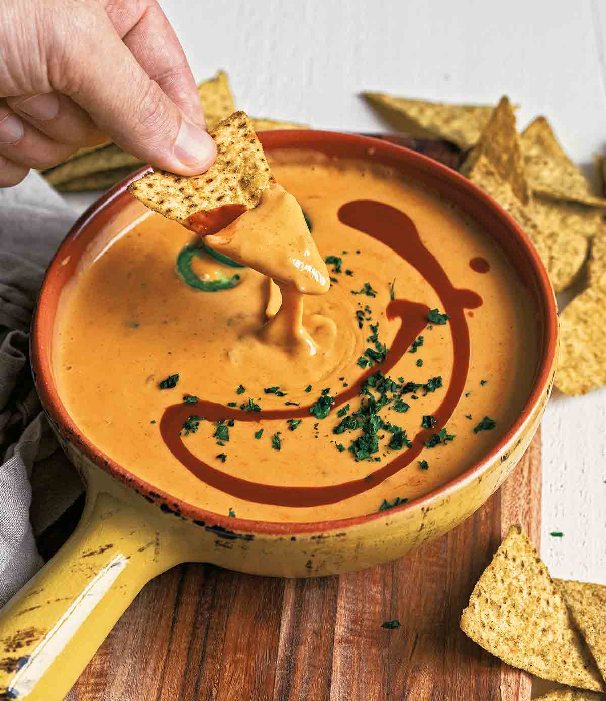 A bowl of easy queso dip with a person dipping a chip into it