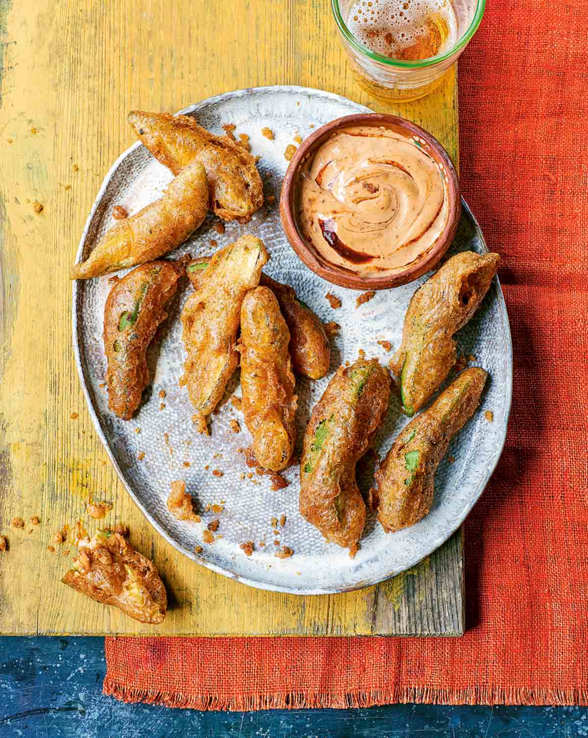 Nine fried avocado dippers on a silver platter with a small dish of chipotle dipping sauce beside them