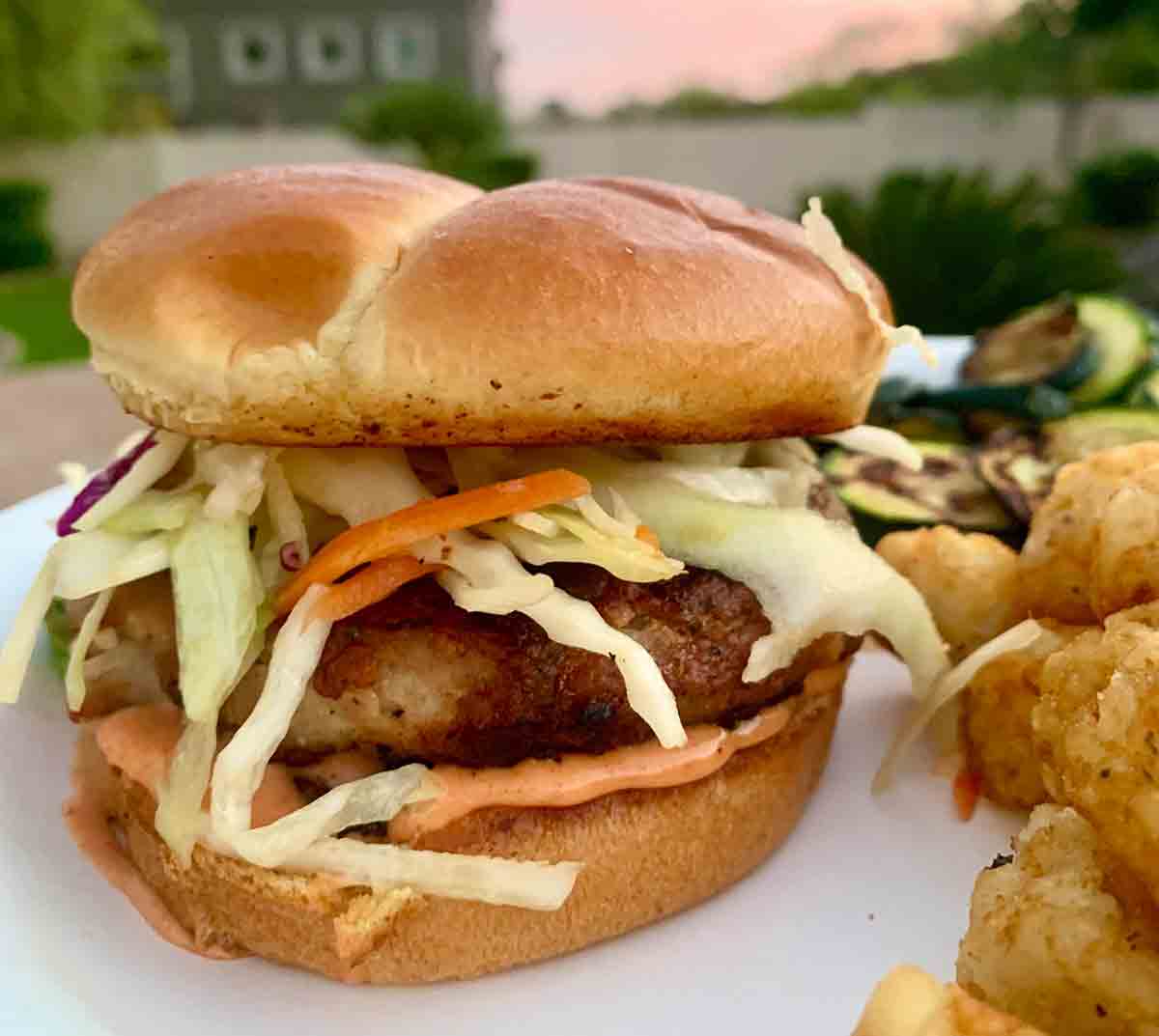 A grilled pork burger topped with coleslaw and tater tots on the side.