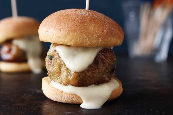 Two ground chicken meatballs on slider buns with a toothpick skewered through them.
