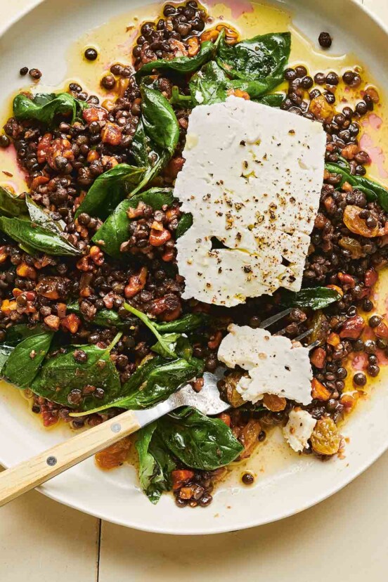 A white bowl filled with warm marinated lentil salad with feta cheese slabs on top.