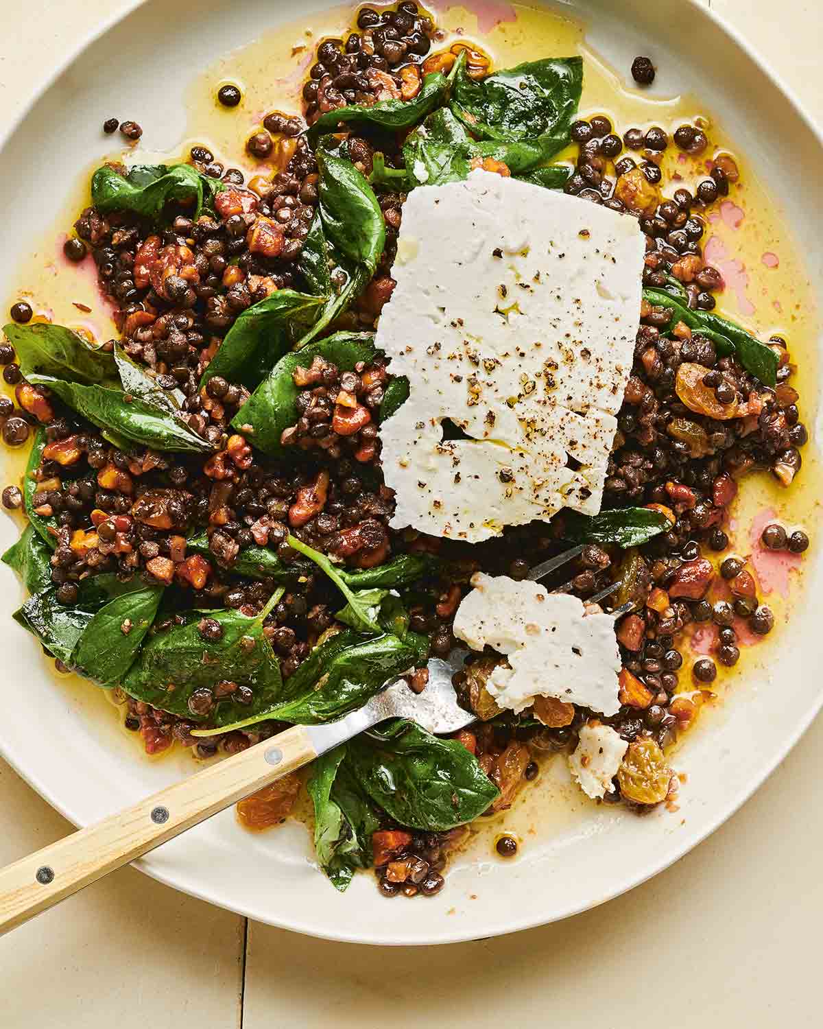 A white bowl filled with warm marinated lentil salad with feta cheese slabs on top.