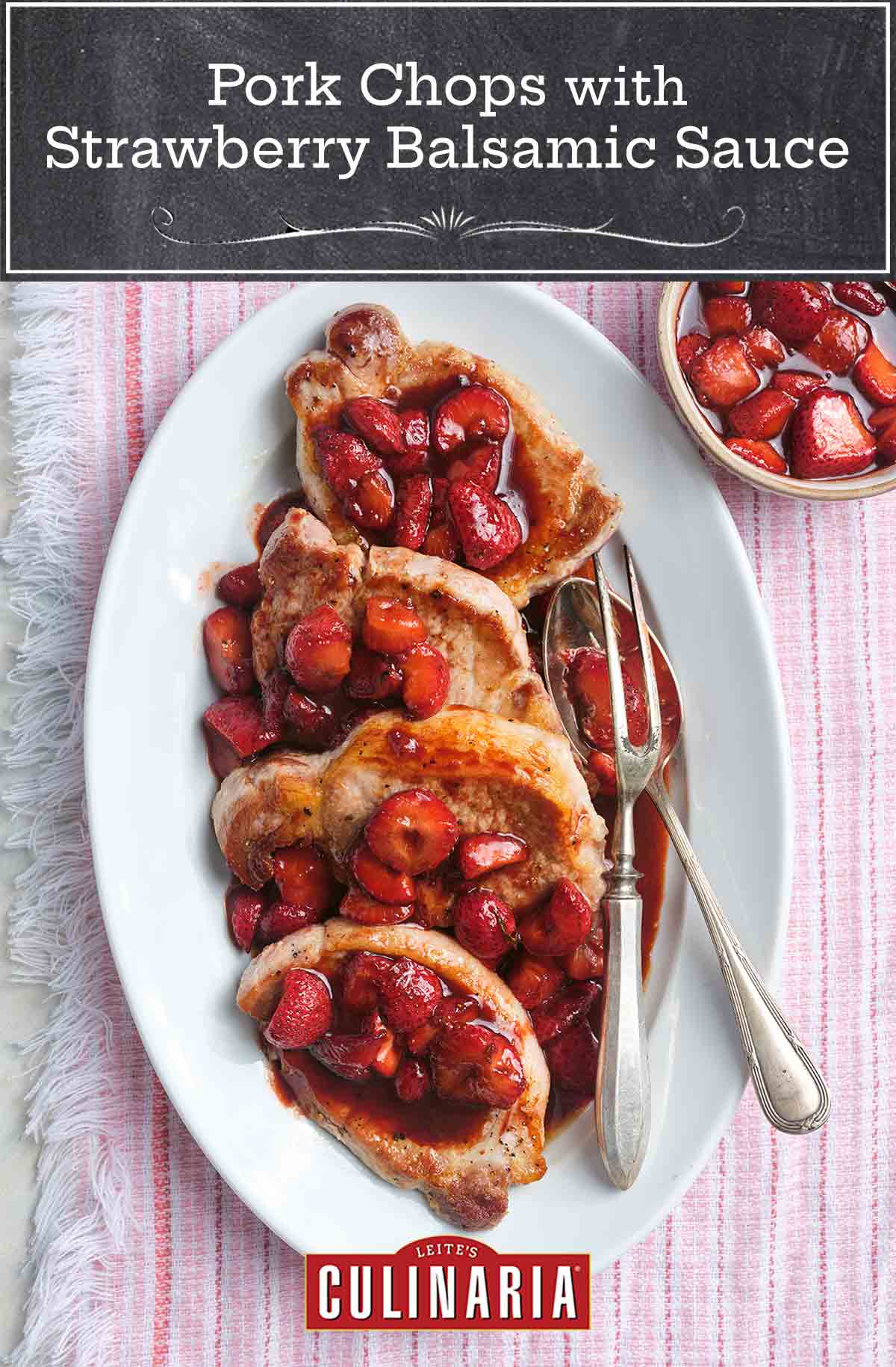 Four pork chops with strawberry balsamic glaze on top arranged on a white oval platter with serving utensils and a bowl of strawberry glaze on the side.
