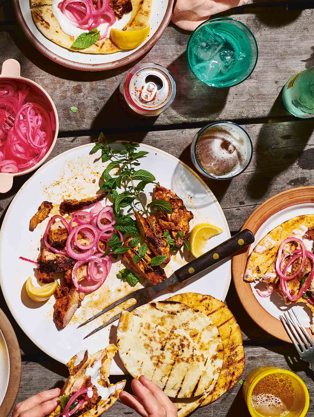 A platter of grilled boneless chicken thighs topped with pickled red onion, mint, lemon, and pita on the side.