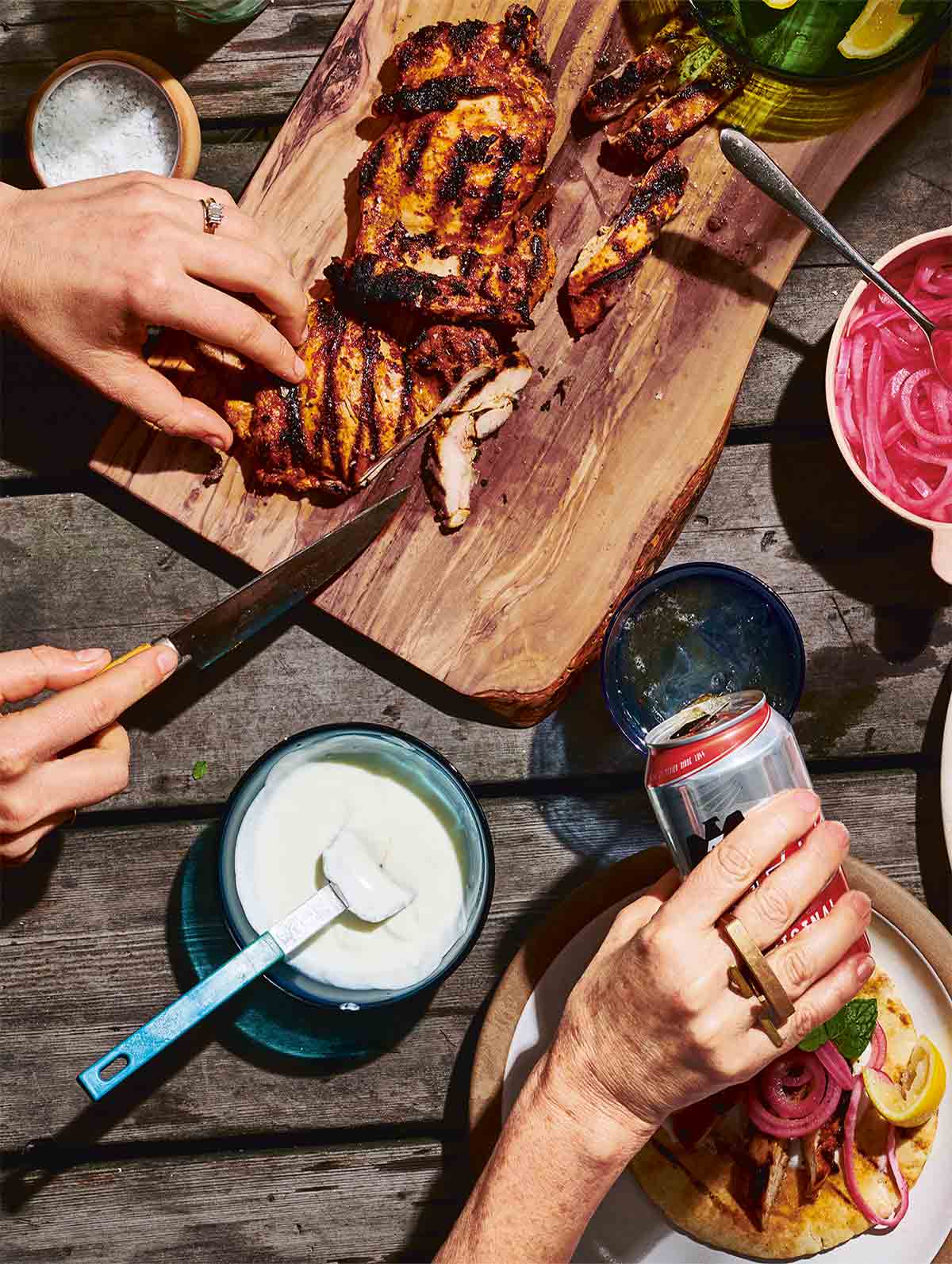 A person carving spiced grilled boneless chicken thighs on a wooden platter.