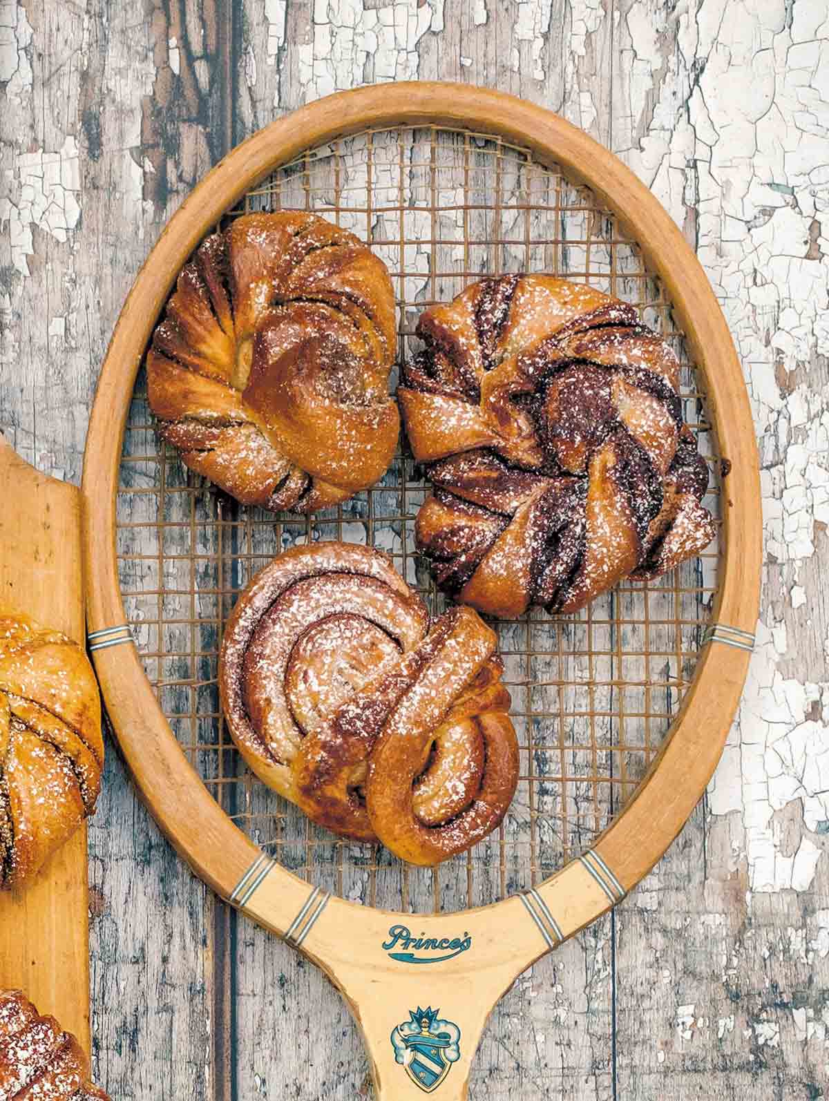 Three Swedish cardamom buns with different fillings laying on an old-fashioned tennis racket.