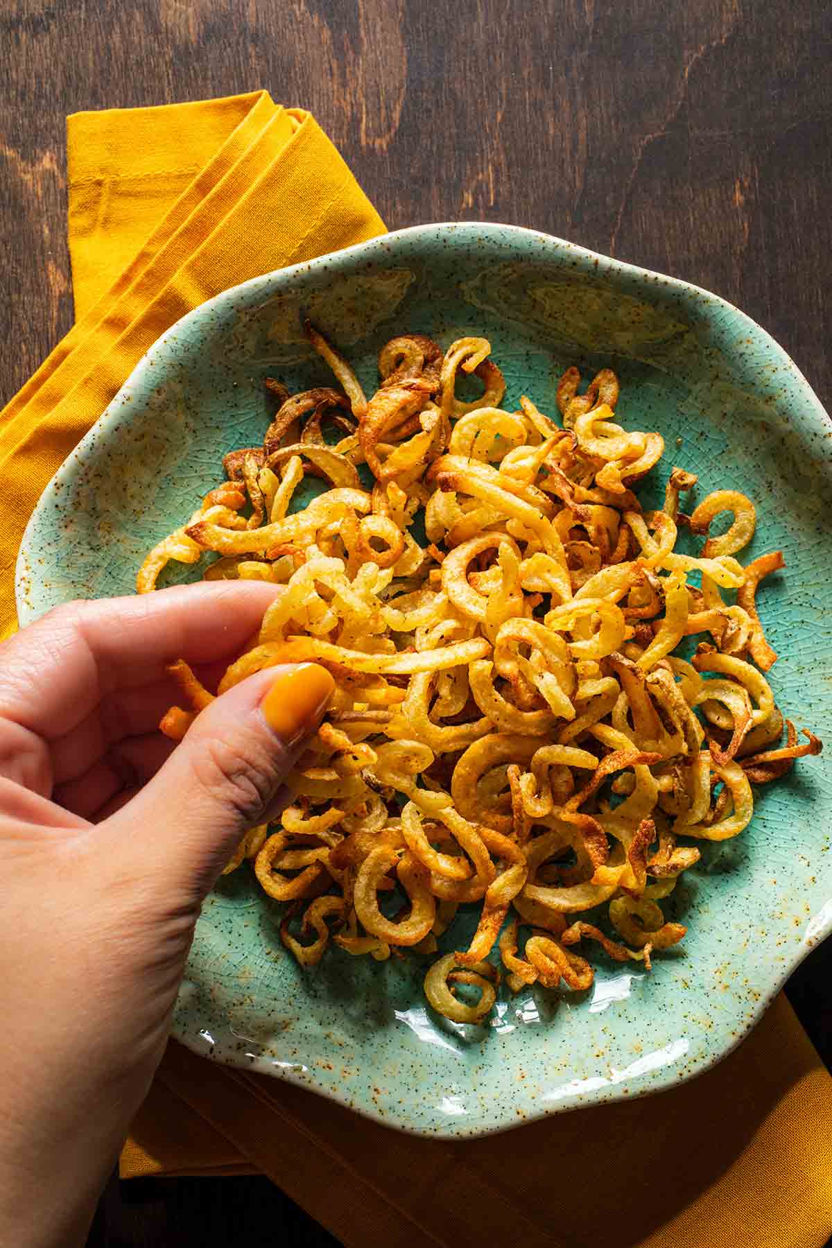 A green bowl filled with air fryer shoestring fries with a person picking some out of it.
