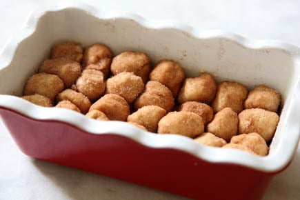 A red ceramic bread pan with dough balls of monkey bread inside.