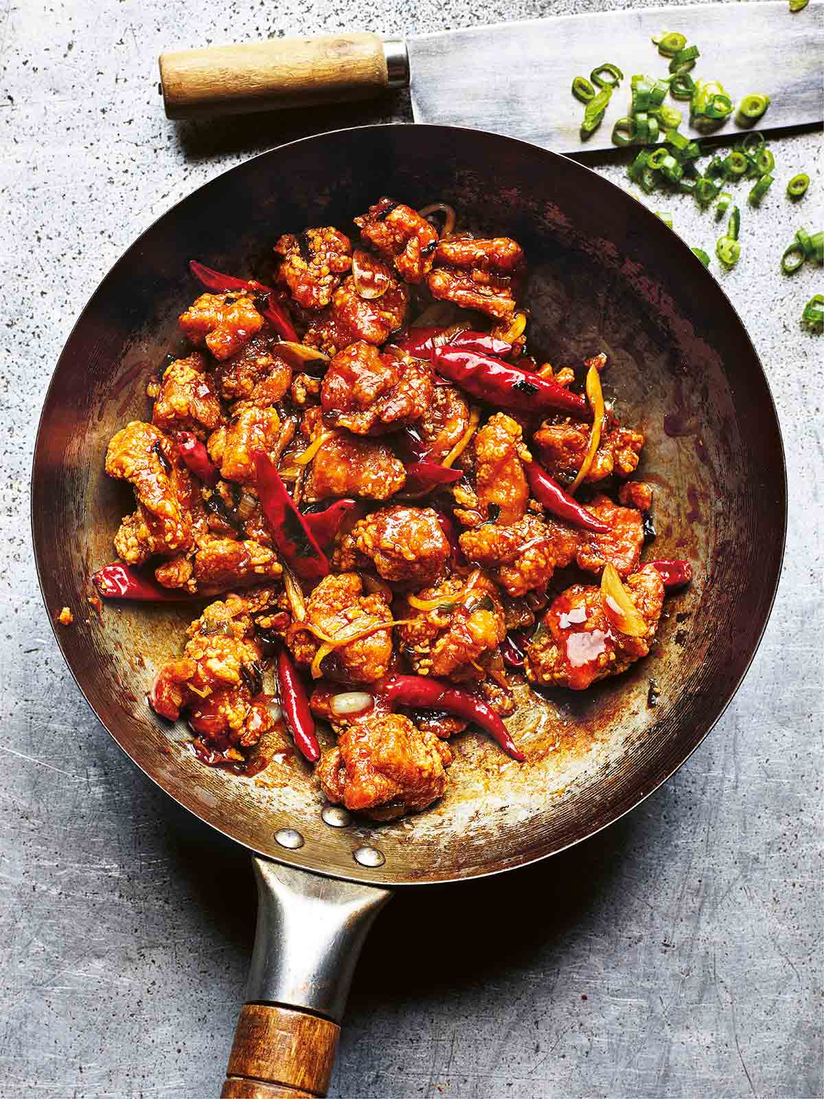 A wok filled with authentic General Tso's chicken with a knife and sliced scallions on the side.