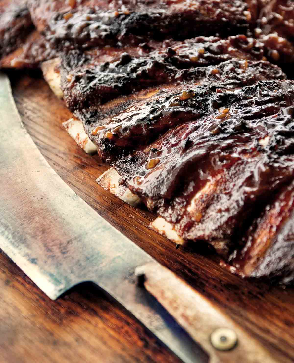 A knife lying next to a slab of barbecue beef ribs.