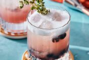 Two short glasses of blueberry prosecco spritz on coasters with thyme sprigs for garnish.