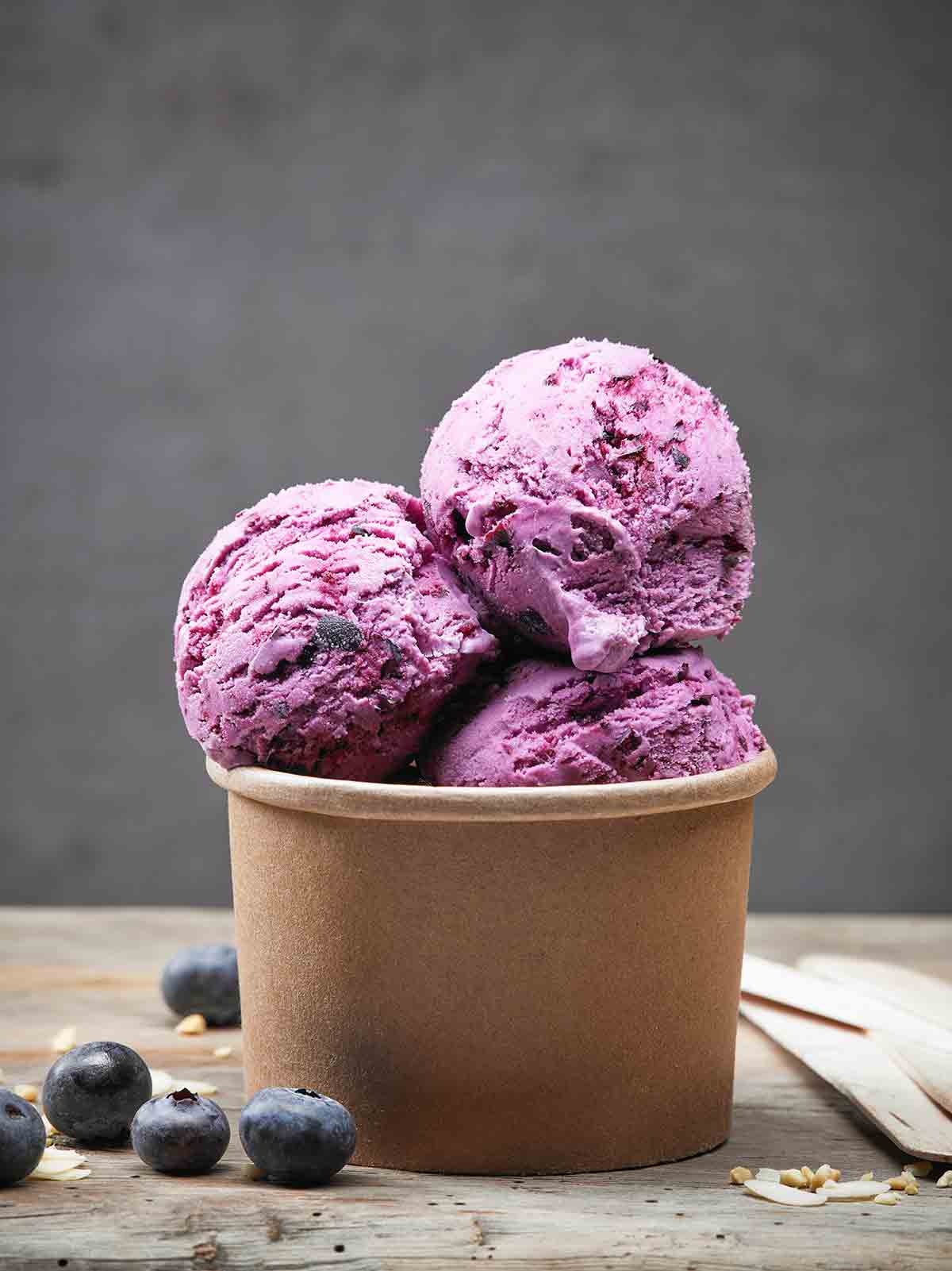 A brown container with three scoops of blueberry ice cream, in the back a stack of containers